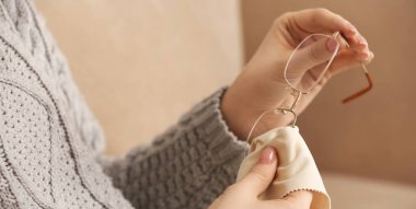 Young woman wiping eyeglasses at home, closeup