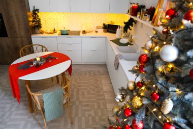 Mutfağın içinde tezgahlar, yemek masası ve Noel ağacı var.