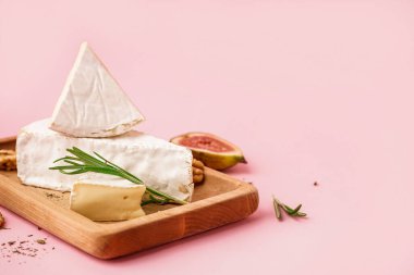 Pembe arka planda lezzetli Camembert peyniri parçaları olan ahşap tahta.