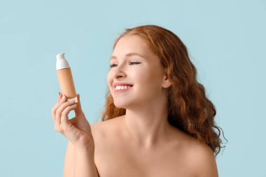 Mavi arka planda makyaj vakfı olan genç kızıl saçlı kadın, yakın plan.