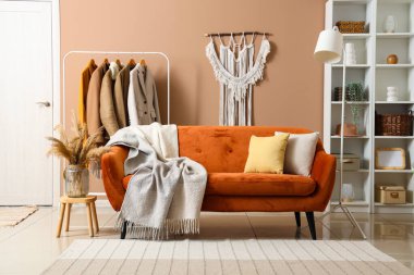 Modern oturma odasının içinde kahverengi kanepe, sıcak battaniye ve askıda asılı giysiler.