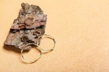 Altın küpeli ağaç kabuğu ve bej arka planda yüzük, yakın plan.