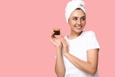 Pembe arka planda krema kavanozu olan genç bir kadın