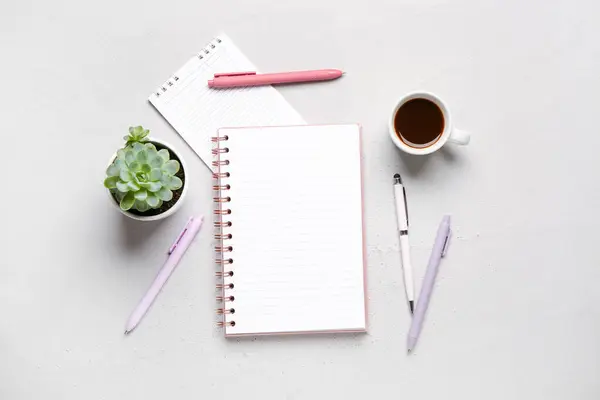 Notebooks with pens and cup of tasty coffee on grey background