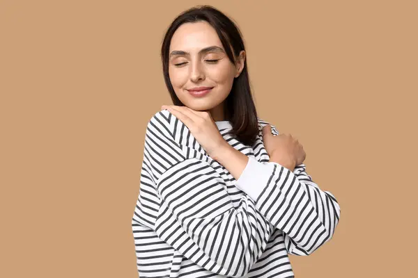 Young woman hugging herself on brown background