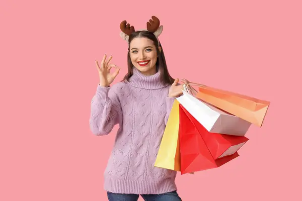ショッピングバッグを持っている若い女性とピンクの背景にOkを示す — ストック写真