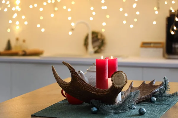 Moose antler with burning candles and Christmas branches on table in kitchen, closeup