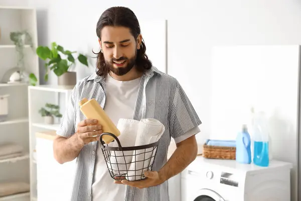 Young man with laundry basket and detergent at home