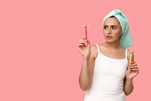 Worried young woman with razors on pink background