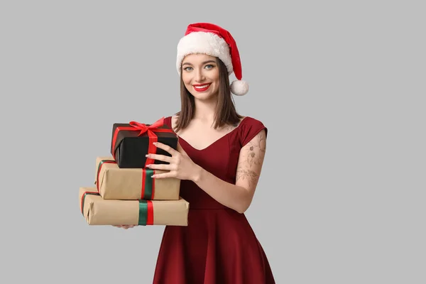 サンタハットの若い女性 灰色の背景にクリスマスギフトボックス — ストック写真