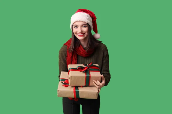 緑の背景にクリスマスギフトボックスとサンタの帽子の若い女性 — ストック写真