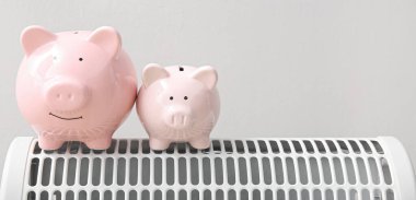 Piggy bankaları elektrikli ısıtıcıya karşı gri arkaplan ve metin için alan. Isıtma kaydetme kavramı