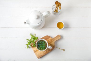 Çaydanlık taze nane çayı, bal ve beyaz ahşap arka planda kaşıklar.