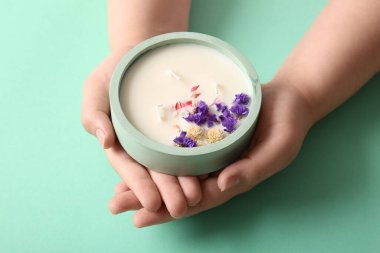 Turkuaz arka planda çiçekli mum tutan kadın eller