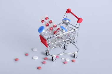 Gri arka planda farklı haplar olan mini alışveriş arabası.