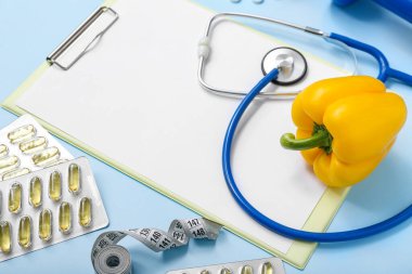 Renk arkaplanında boş pano, hap, steteskop ve dolma biber içeren kompozisyon, yakın plan