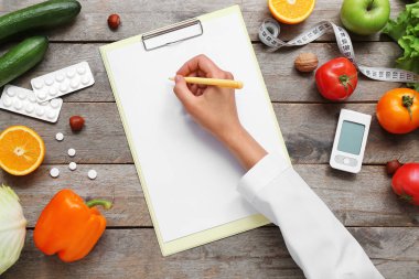 Boş pano, glukometre ve ahşap zemin üzerinde sağlıklı ürünler olan kadın doktor eli.