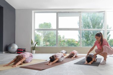 Beden eğitimi hocasıyla yoga yapan bir grup çocuk.