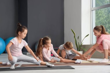 Beden eğitimi hocasıyla yoga yapan bir grup çocuk.