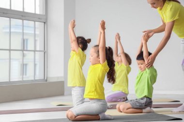 Eğitmeni olan bir grup küçük çocuk spor salonunda yoga yapıyor.