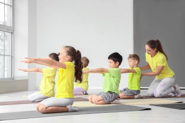 Eğitmeni olan bir grup küçük çocuk spor salonunda yoga yapıyor.