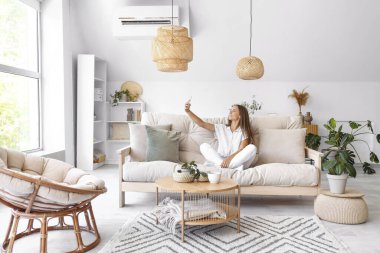 Cep telefonlu genç bir kadın oturma odasında selfie çekiyor.