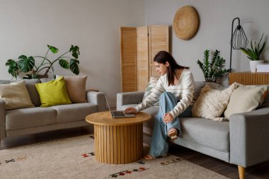 oturma odasında kanepede dizüstü kullanan genç kadın