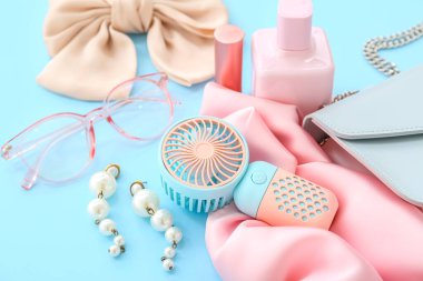 Mavi arka planda taşınabilir elektrikli yelpaze ve şık bayan aksesuarları olan kompozisyon, yakın plan.