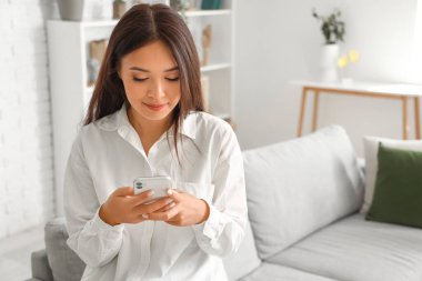 Oturma odasında cep telefonu kullanan güzel bir Asyalı kadın.