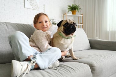 Evdeki kanepede oturan sevimli köpekli küçük kız.