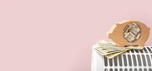 Piggy bank and money on electric heater against pink background with space for text. Heating saving concept