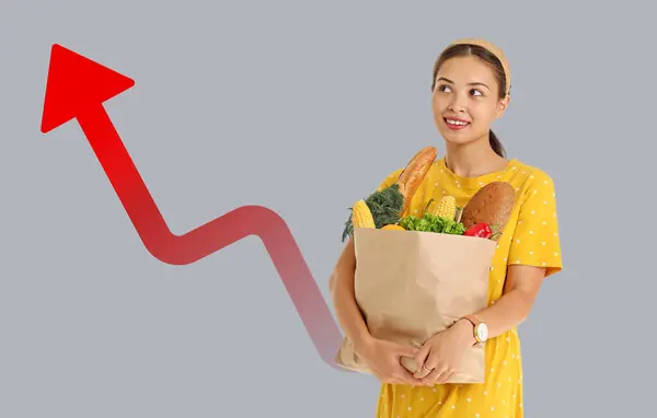Woman holding shopping bag with products on grey background. Food price increase