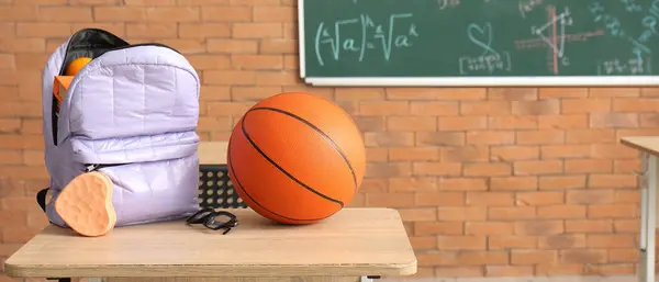 School backpack and ball on desk in classroom