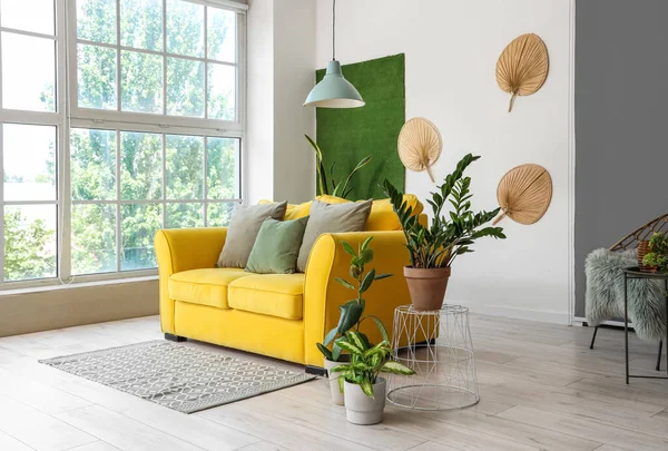 Interior of light living room with yellow sofa and houseplants