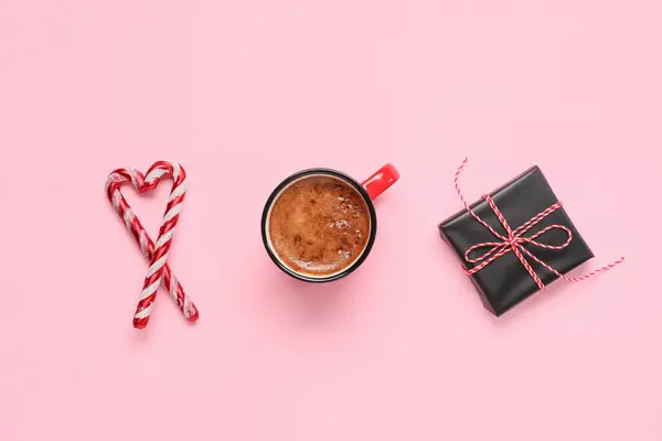 Mug of coffee with gift box and candy canes on pink background