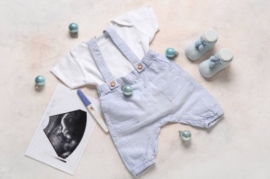 Şık bebek kıyafetleri, sonogram görüntüsü ve açık arkaplanda Noel topları olan kompozisyon