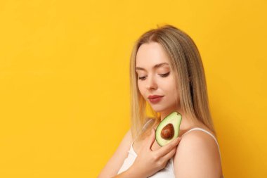 Sarı arka planda avokadosu olan genç bir kadın, yakın plan.