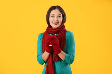 Sarı arka planda bir fincan kahveyle sıcak eşarplı güzel bir Asyalı kadın.