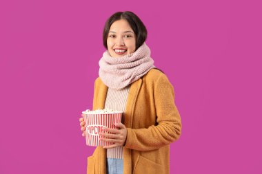 Mor arka planda patlamış mısırlı, sıcak eşarplı güzel bir Asyalı kadın.