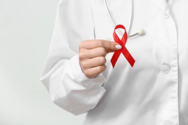 Beyaz arka planda kırmızı kurdeleli genç bayan doktor, yakın plan. AIDS Günü konsepti