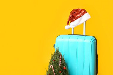 Noel Baba şapkalı bavul ve sarı arka planda Noel ağacı.