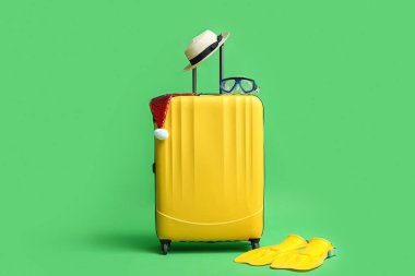 Plaj aksesuarları ve yeşil arka planda Noel Baba şapkası olan renkli bavul.