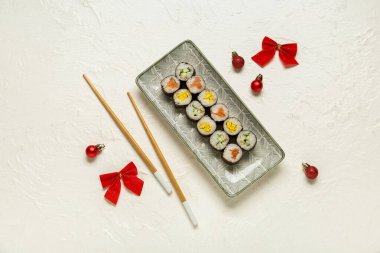 Lezzetli suşi ruloları ve beyaz arka planda Noel dekoru olan bir tabak.