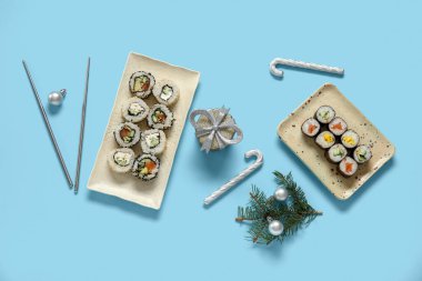 Lezzetli suşi ruloları ve mavi arka planda Noel dekoru olan tabaklar.