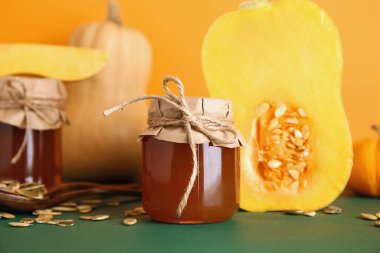 Tatlı balkabağı reçeli kavanozları ve renkli arka planda tohumlar.