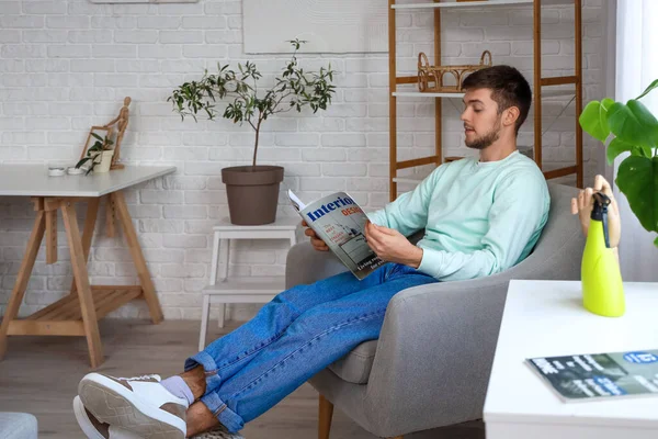 stock image Young bearded man reading magazine in armchair at home