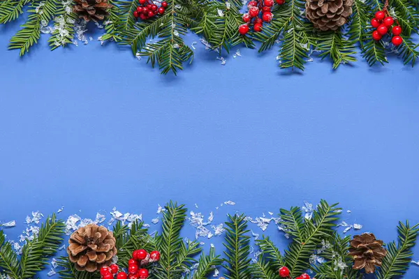 Mavi arka planda köknar dalları, koniler ve kırmızı böğürtlenlerle güzel bir Noel kompozisyonu