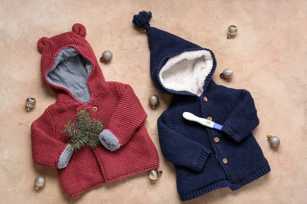 Bebek kıyafetleri, hamilelik testi ve renk arkaplanı üzerine Noel süslemeleri içeren kompozisyon