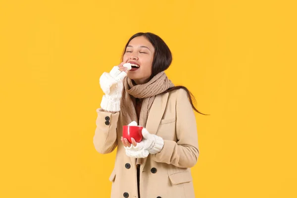 年轻美丽的亚洲女人 戴着温暖的围巾 手里拿着一杯黄色背景的棉花糖可可 — 图库照片