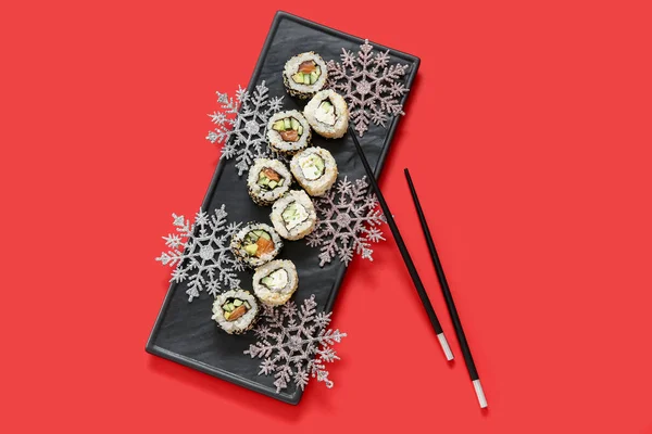 赤い背景のクリスマスパーティーのためのおいしい寿司ロールと雪片とプレート — ストック写真